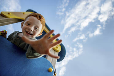 Lächelnder Junge auf einem Spielgerät mit Palme unter dem Himmel - MBLF00085
