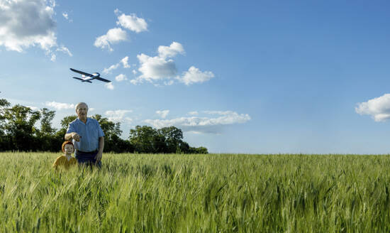 Großvater und Enkel spielen mit einem Spielzeugflugzeug auf einem Feld - MBLF00095