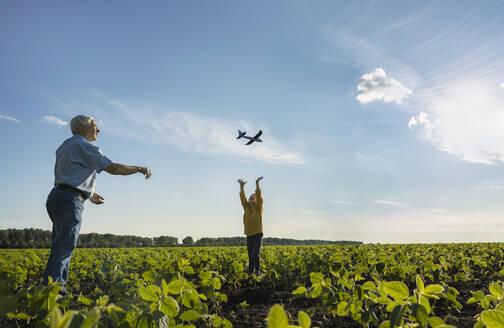 Großvater fliegt Spielzeugflugzeug mit Enkel, der sich auf einem Feld vergnügt - MBLF00105