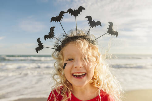 Glückliches Mädchen trägt Halloween-Stirnband mit Fledermäusen am Strand - SIF01069