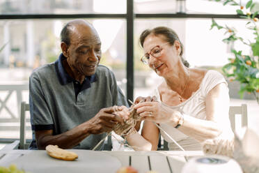 Senior woman teaching crochet to male friend at nursing home - MASF40181