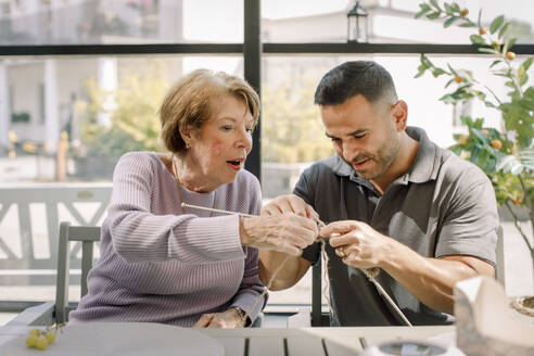 Senior woman and male nurse crocheting together at retirement home - MASF40183