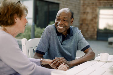 Happy senior man talking to woman while sitting at dining table - MASF40191