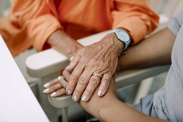 Midsection of female nurse and senior woman consoling while sitting with holding hands - MASF40195