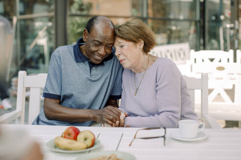 Senior man and woman holding hands while sitting at dining table - MASF40199