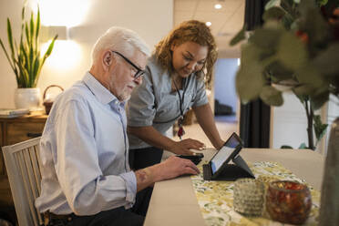 Young female caregiver assisting senior man in using digital tablet at retirement home - MASF40213