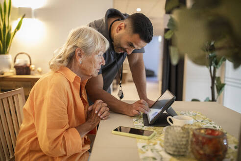 Male nurse assisting senior woman in using digital tablet at nursing home - MASF40215