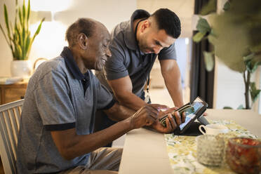 Male nurse assisting senior man in using digital tablet and smart phone at nursing home - MASF40216