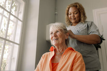 Low angle view of young female caregiver braiding senior woman's hair at nursing home - MASF40219
