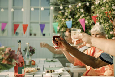 Men and women raising toast while sitting at dining table in retirement home - MASF40256