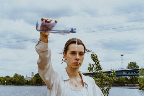 Porträt einer selbstbewussten jungen nicht-binären Person, die Wasser aus einer Flasche gegen den Himmel gießt - MASF40275
