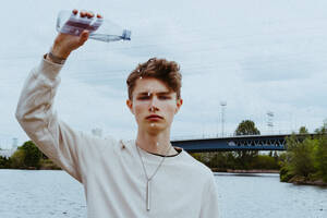 Porträt eines selbstbewussten jungen Mannes, der Wasser aus einer Flasche in den Himmel gießt - MASF40282