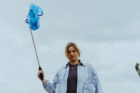 Low angle portrait of confident young woman collecting garbage against sky - MASF40287