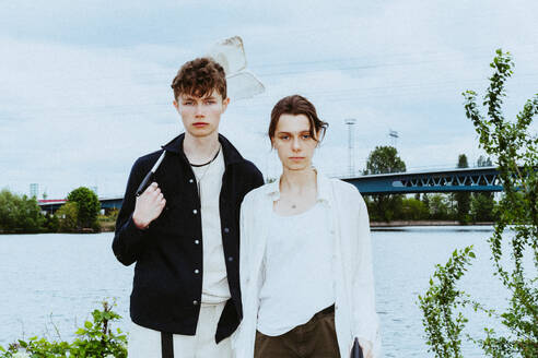 Portrait of young friends collecting plastic garbage near river against sky - MASF40290