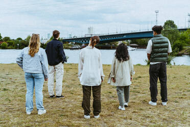 Full length rear view of young friends standing near river - MASF40296