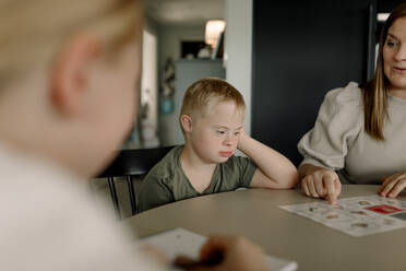 Boy with down syndrome sitting by mother teaching at home - MASF40312