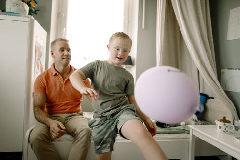 Man sitting behind boy with down syndrome playing with balloon - MASF40315