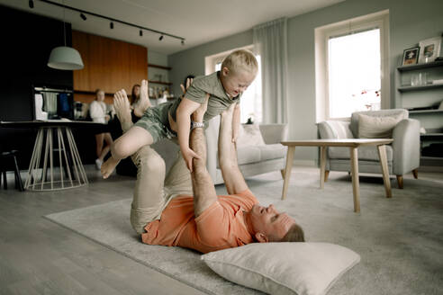Full length of father lying on carpet while lifting son in living room at home - MASF40317