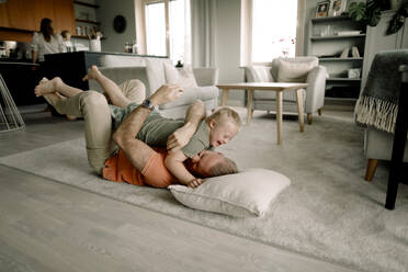 Full length of father lying on carpet while embracing son in living room at home - MASF40318