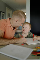 Father assisting son with down syndrome in studying at dining table - MASF40319