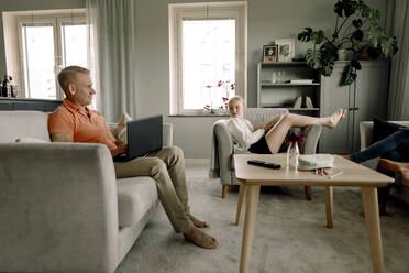 Full length of father and daughter looking at each other in living room - MASF40336