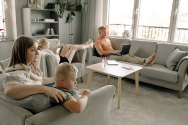 Mother and son with down syndrome watching TV while man and daughter sitting in living room at home - MASF40337