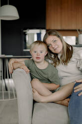 Porträt von Mutter und Sohn mit Down-Syndrom, die zu Hause auf dem Sofa sitzen - MASF40339