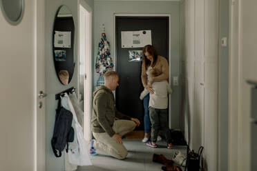 Boy embracing mother by father kneeling in mudroom at home - MASF40343