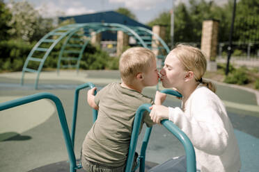 Sibling kissing at carousel in park on sunny day - MASF40346