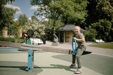 Volle Länge Seitenansicht Porträt des glücklichen Jungen mit Down-Syndrom genießen Wippe im Park - MASF40350