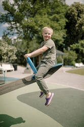 Full length side view of boy with down syndrome enjoying seesaw at park - MASF40352