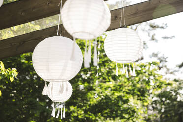 Low angle view of white lanterns hanging from pergola at patio - MASF40363