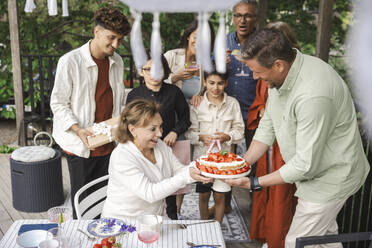 Family celebrating midsummer with cake at patio - MASF40398