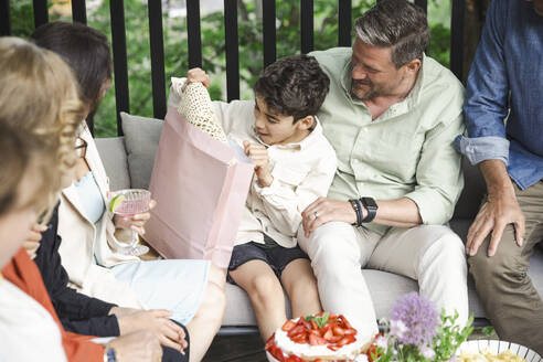 Surprised boy opening gift with family in patio - MASF40404