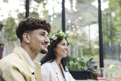 Smiling man sitting by woman wearing tiara at dinner party - MASF40433