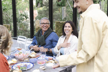 Cheerful family listening to young man talking during dinner party - MASF40436