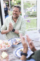 Cheerful mature man clapping while sitting at dining table - MASF40437
