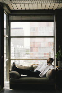 Full length of lonely depressed mature businessman reclining on sofa at office - MASF40446