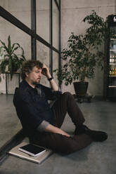 Side view of depressed professional businessman leaning on glass wall at office - MASF40468