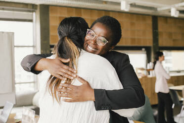 Happy businesswoman embracing non-binary colleague at office - MASF40474