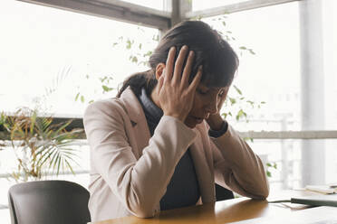 Exhausted businesswoman sitting with head in hands at office - MASF40477
