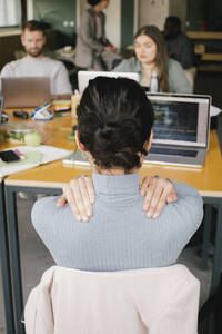 Rear view of exhausted businesswoman rubbing shoulders while working at office - MASF40478