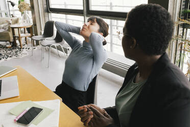 Businesswoman sitting besides overworked female colleague struggling with pain at office - MASF40479