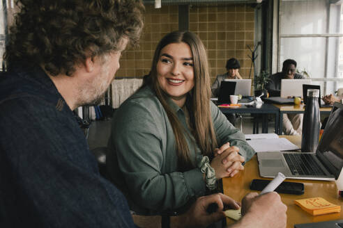 Smiling male business professional discussing with colleague at office - MASF40483