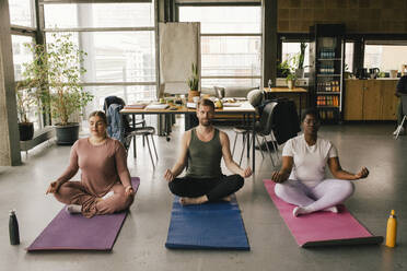 Full length of multiracial colleagues meditating together on mats at office - MASF40490