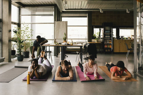 Colleagues lying on exercise mats in office - MASF40495