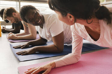 Smiling businesswoman practicing plank position with colleagues on exercise mats at office - MASF40498