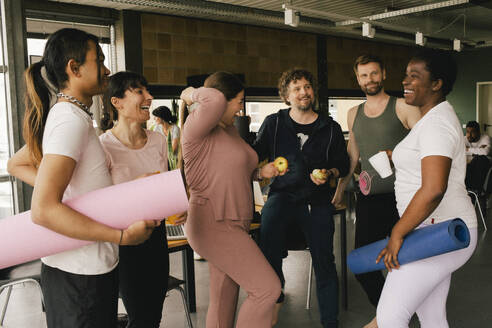 Happy multiracial colleagues standing with yoga mats and fruits in workplace - MASF40509