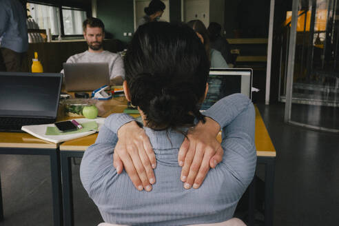 Rear view of exhausted businesswoman rubbing shoulders while sitting at workplace - MASF40518