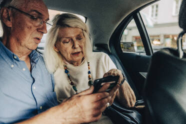 Senior couple using smart phone while sitting in taxi - MASF40530